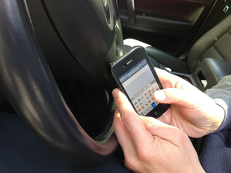 A photo of a person texts while driving.