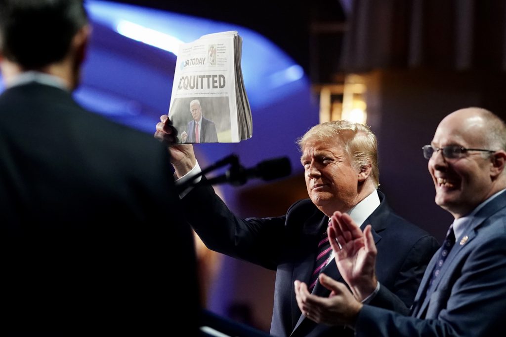 President Trump holds up a newspaper with the word "Acquitted" blairing across the headline.